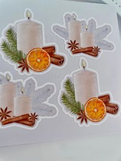 three stickers with candles and cinnamons on them, one has an orange slice