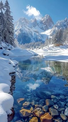 a mountain lake surrounded by snow covered trees and rocks in the foreground with mountains in the background