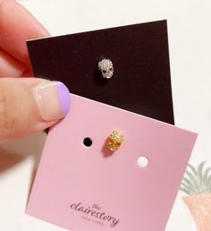 a hand holding a pair of earrings in front of a pink card with black and white designs on it