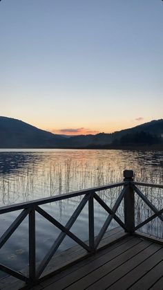 the sun is setting over a lake with mountains in the background and a wooden bridge leading to it