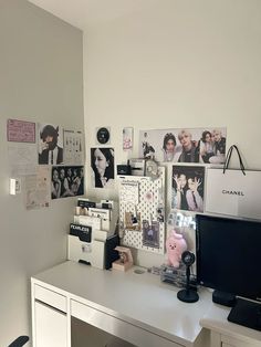 a white desk topped with a computer monitor next to a wall covered in pictures and photos