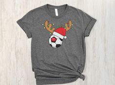 When you love Christmas and Soccer! This ultra cotton tee is a classic. Quality cotton construction means that designs are sure to shine. The shoulders are tapped for a good upper-body fit. There are no side seams, ensuring a clean, unbroken flow. The collar has ribbed knitting for improved elasticity. The materials that went into this product are sustainably sourced and economically friendly.  100% cotton Classic fit Tear-away label Runs bigger than usual Soccer Christmas Shirts, Golden Girls Gifts, Girls Cup, Soccer Tees, Balls Shirt, Soccer Shirt, Love Christmas, Reindeer Christmas, Soccer Mom