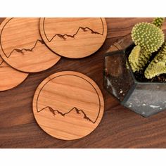 three wooden coasters with mountains on them next to a cacti and succulent