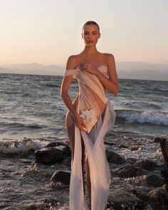 a woman standing on top of a beach next to the ocean wearing a sheer dress