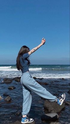 a woman standing on top of rocks near the ocean with her arms in the air