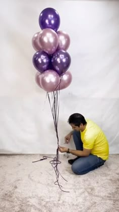 a man kneeling down next to a bunch of balloons