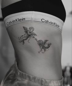 a woman's stomach with two cherubs tattooed on the side by her