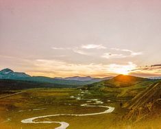 the sun is setting over a valley with a river running through it and mountains in the distance