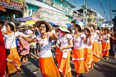 a group of women in orange dresses and hats dance on the street while people watch