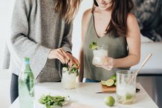 two women standing at a table with drinks and limes in front of the counter