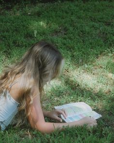 a woman laying on the grass reading a book with her hair blowing in the wind