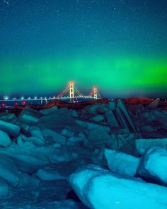 the aurora bridge is lit up in green and blue as it sits above ice covered rocks