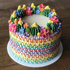 a multicolored cake on a white plate sitting on top of a wooden table