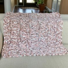 a couch with a pink and white blanket on top of it next to a potted plant