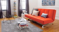 a living room with an orange couch and bookshelves on the floor in front of windows