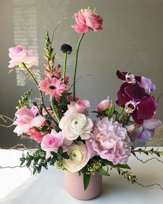 a vase filled with pink and white flowers on top of a table next to a wall