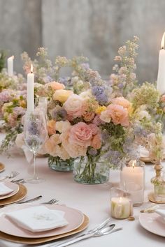 the table is set with candles and flowers in vases, plates and napkins