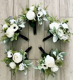 a wreath with white flowers and greenery arranged in the shape of a heart on a wooden floor