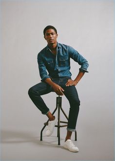 a man sitting on top of a stool wearing white shoes and blue shirt with jeans