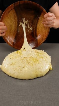 a person holding a wooden bowl over a doughnut that has been kneaded