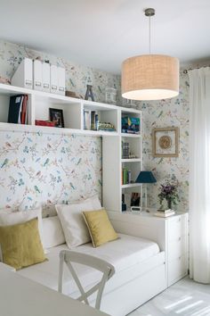 a white bed sitting under a lamp next to a book shelf filled with lots of books