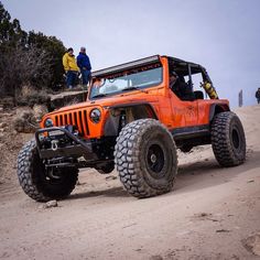 an orange jeep driving down a dirt road with people standing on the top of it