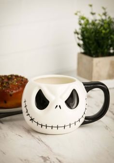 a coffee mug with a face painted on it sitting next to a donut covered in spooky eyes