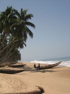 two people standing on the beach next to a boat with palm trees in the background