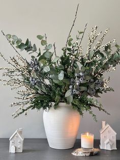 a white vase filled with lots of greenery on top of a table next to a lit candle