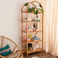 a wooden shelf with plants and books on it next to a wicker chair in front of a window