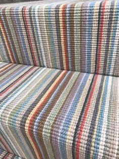 a multicolored striped couch sitting on top of a wooden floor next to a window