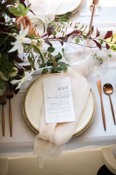 the table is set with white and gold plates, silverware, and greenery