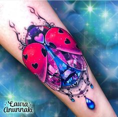 a ladybug tattoo on the arm with blue and pink water drops around it