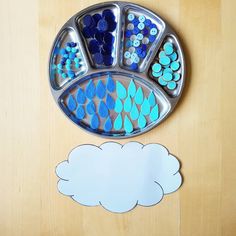 a metal tray with blue and green designs on it next to a cloud shaped paper cutout