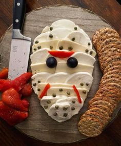 a wooden plate topped with cheese and crackers next to a face shaped like a man