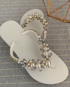 a pair of white flip flops with pearls and crystals on the bottom, sitting on a carpet