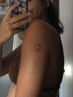 a woman taking a selfie with her cell phone in front of her face and sun tattoo on her arm