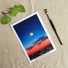 an image of a painting and a brush on a table with a plant next to it