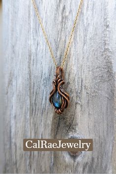 a gold necklace with a blue stone in the center on a wooden background that says, calaver jewelry