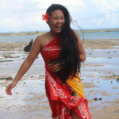 a woman standing on top of a sandy beach next to the ocean wearing a red and yellow dress