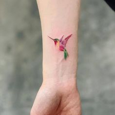 a small hummingbird tattoo on the left inner wrist is shown in pink and green