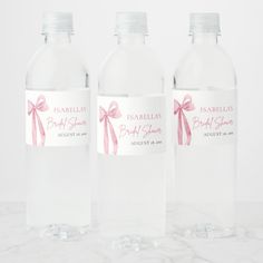 three clear water bottles with pink bows on them