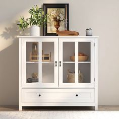 a white cabinet with glass doors and flowers in vases next to bookshelf