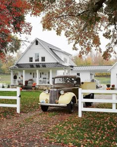 an old car is parked in front of a white house with autumn leaves on the ground