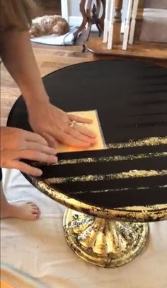 a person is placing something on top of a cake that has been decorated with gold and black stripes