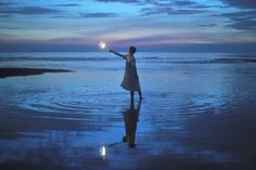 a woman standing on top of a beach holding a light