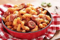 a red bowl filled with pasta and sausage on top of a checkered table cloth