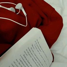 an open book and headphones on top of a red blanket with a white pillow