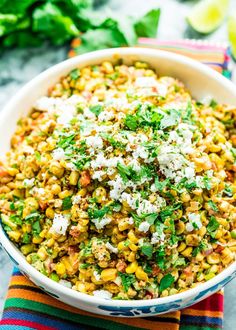 a white bowl filled with mexican street corn and topped with cilantro, parmesan cheese and green onions