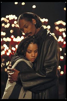 two people embracing each other with lights in the back ground and behind them, one person is wearing a black jacket